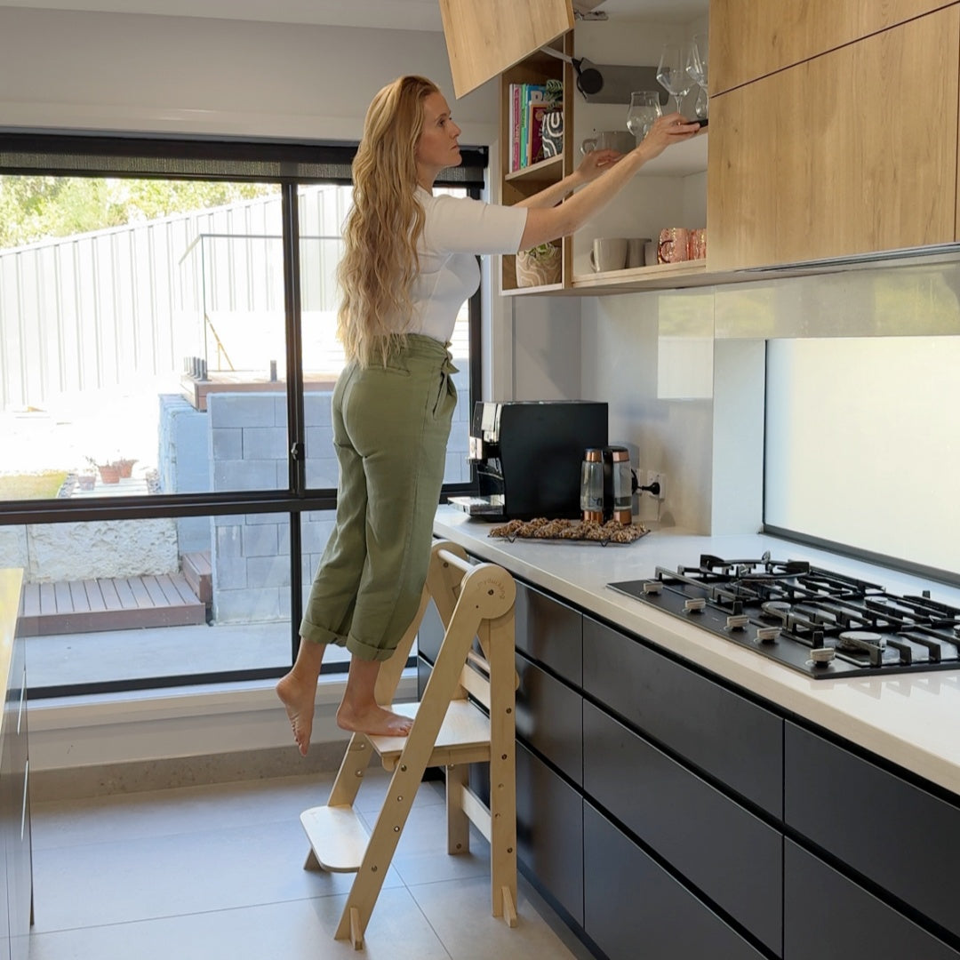 Adult using MILA learning tower as step stool reaching kitchen cabinets - myduckling